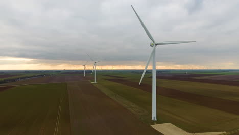 Wind-turbines-aerial-shot-tracking-towards.-Sunset-France-crop-fields-cloudy